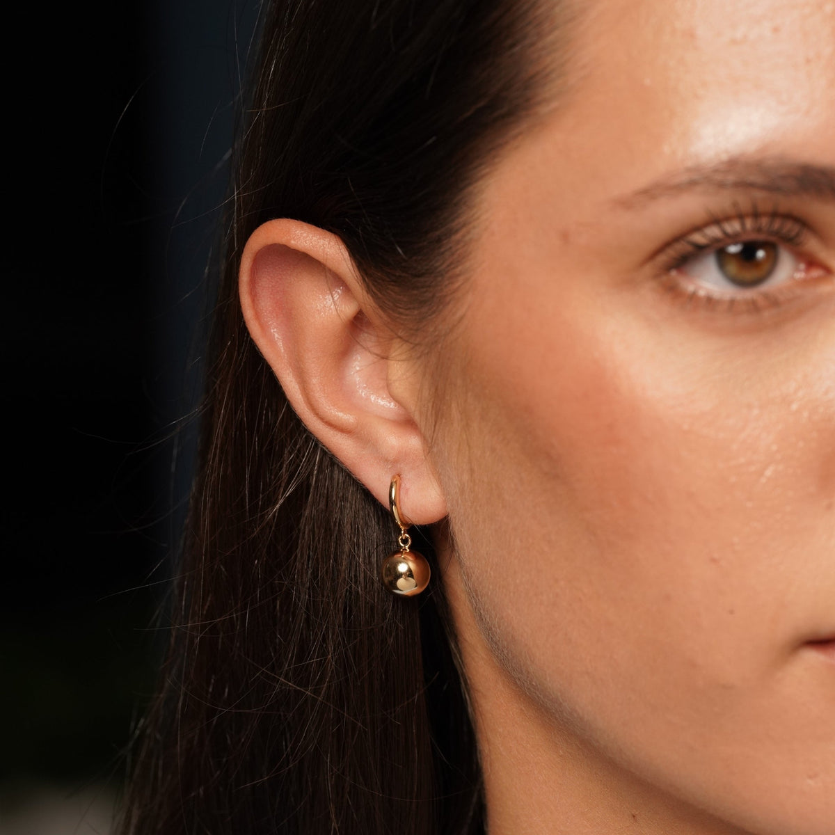 18k Gold plated hoop earring with ball drop, shown on model's ear.