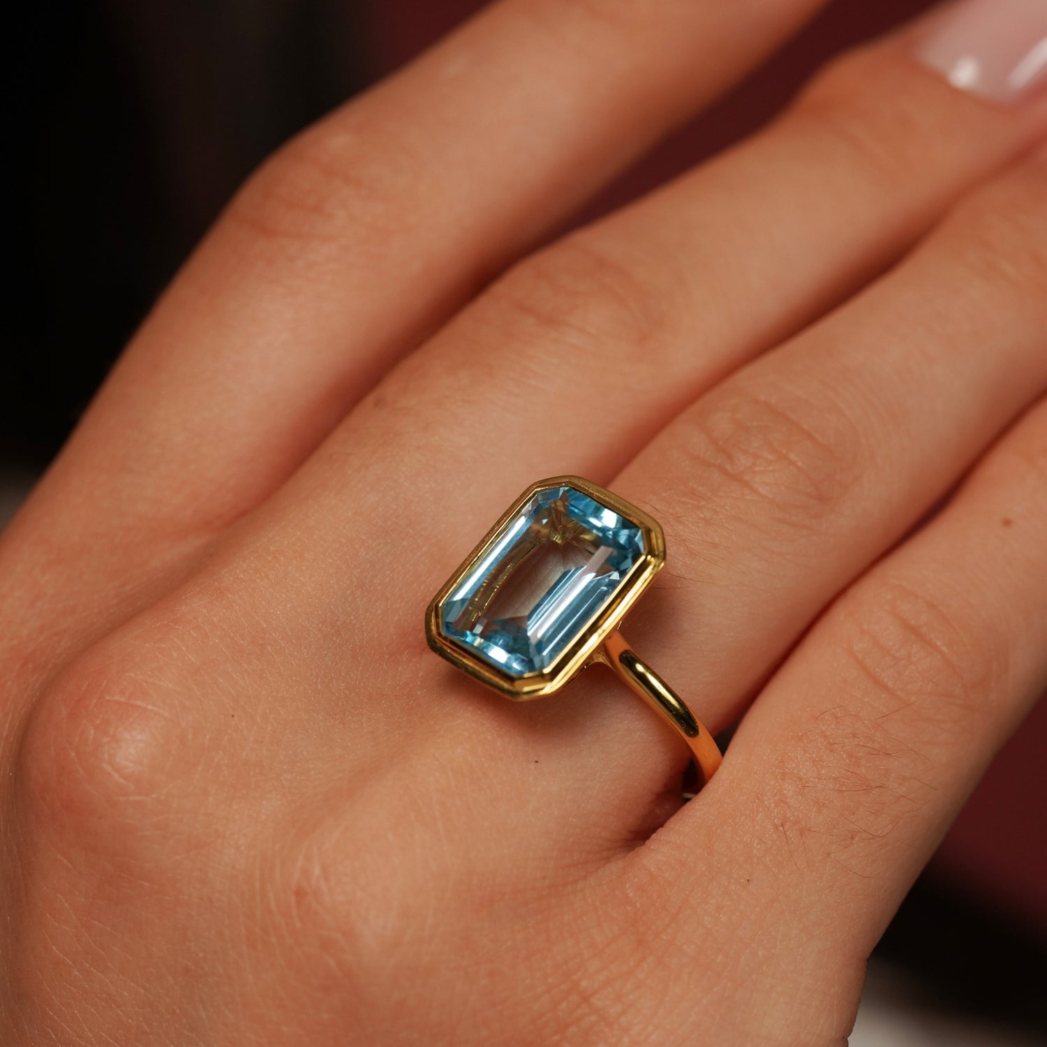 A close-up of a gold ring with a rectangular light blue gemstone worn on a hand.