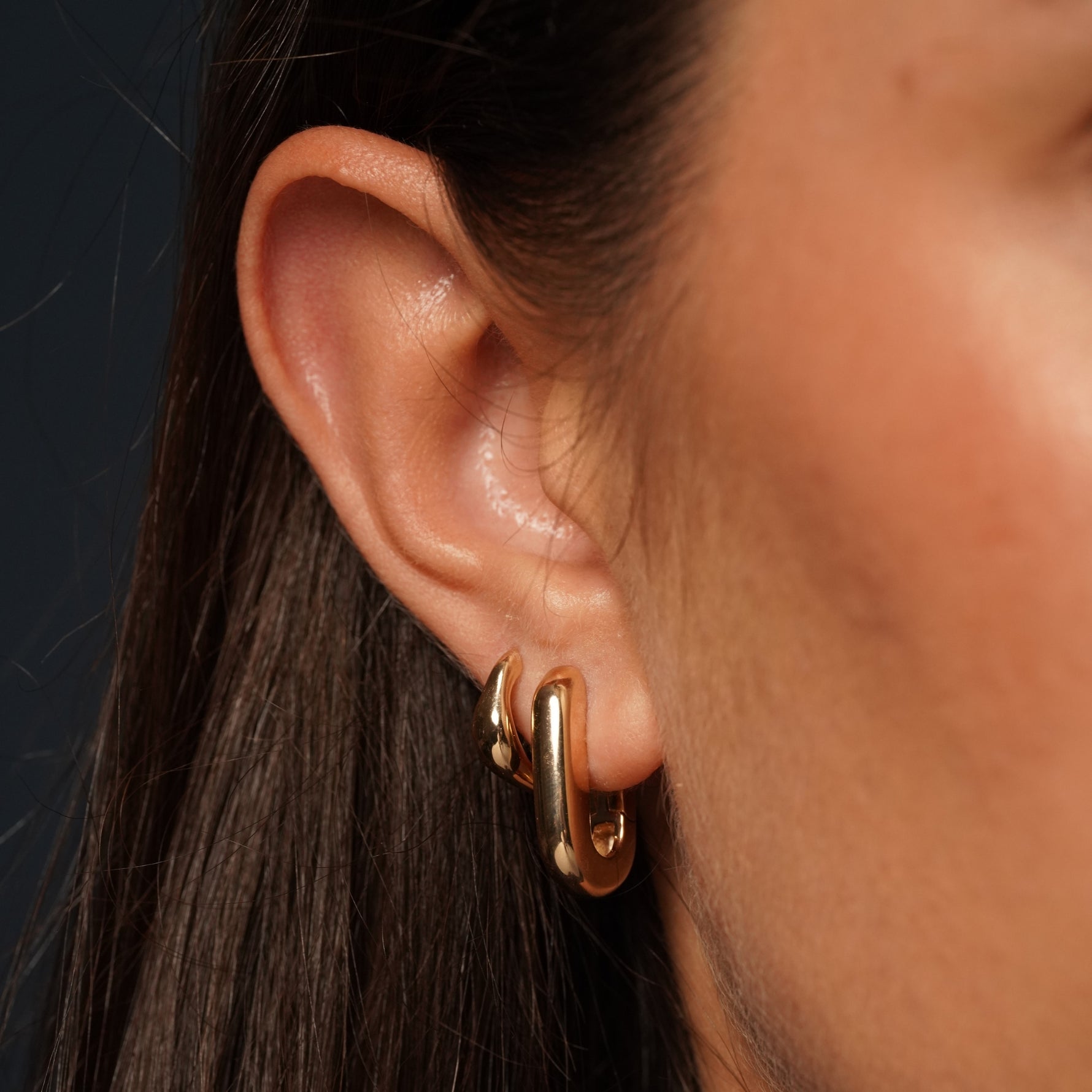 A close-up of a person's ear wearing a pair of chunky, polished champagne gold colour huggie hoop earrings.
