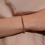 A close-up of a person's wrist wearing a delicate gold chain bracelet against a soft beige fabric background.