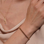 A close-up lifestyle shot of a model wearing a delicate gold chain bracelet on her wrist, along with a matching gold pendant necklace. 