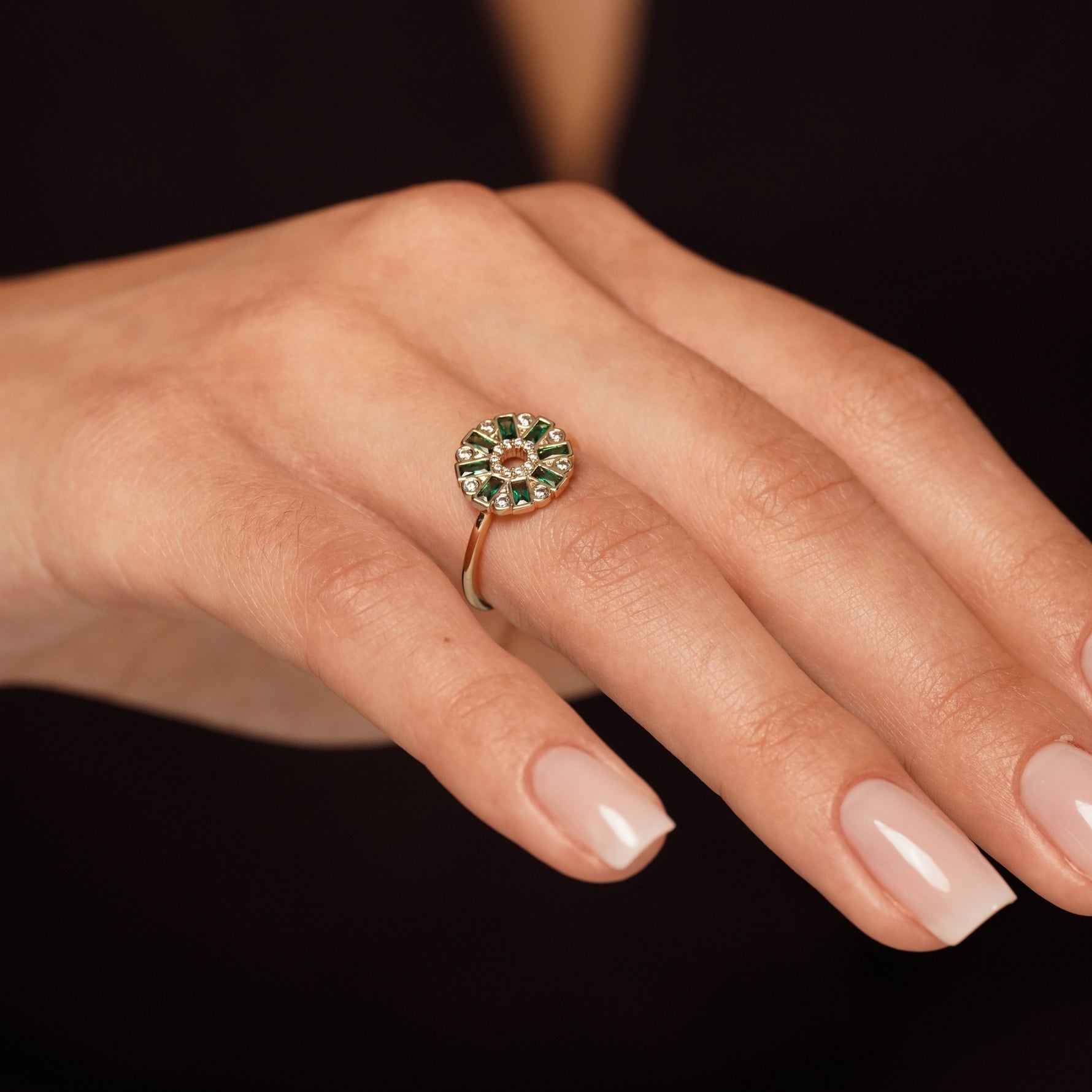 A close-up of a hand wearing Lucky Lady Ring in 18K Gold Plating Featuring Emerald-Coloured Baguette Cubic Zirconia and Clear Round Cubic Zirconia in an Art Deco Sunburst Design | Burren Jewellery
