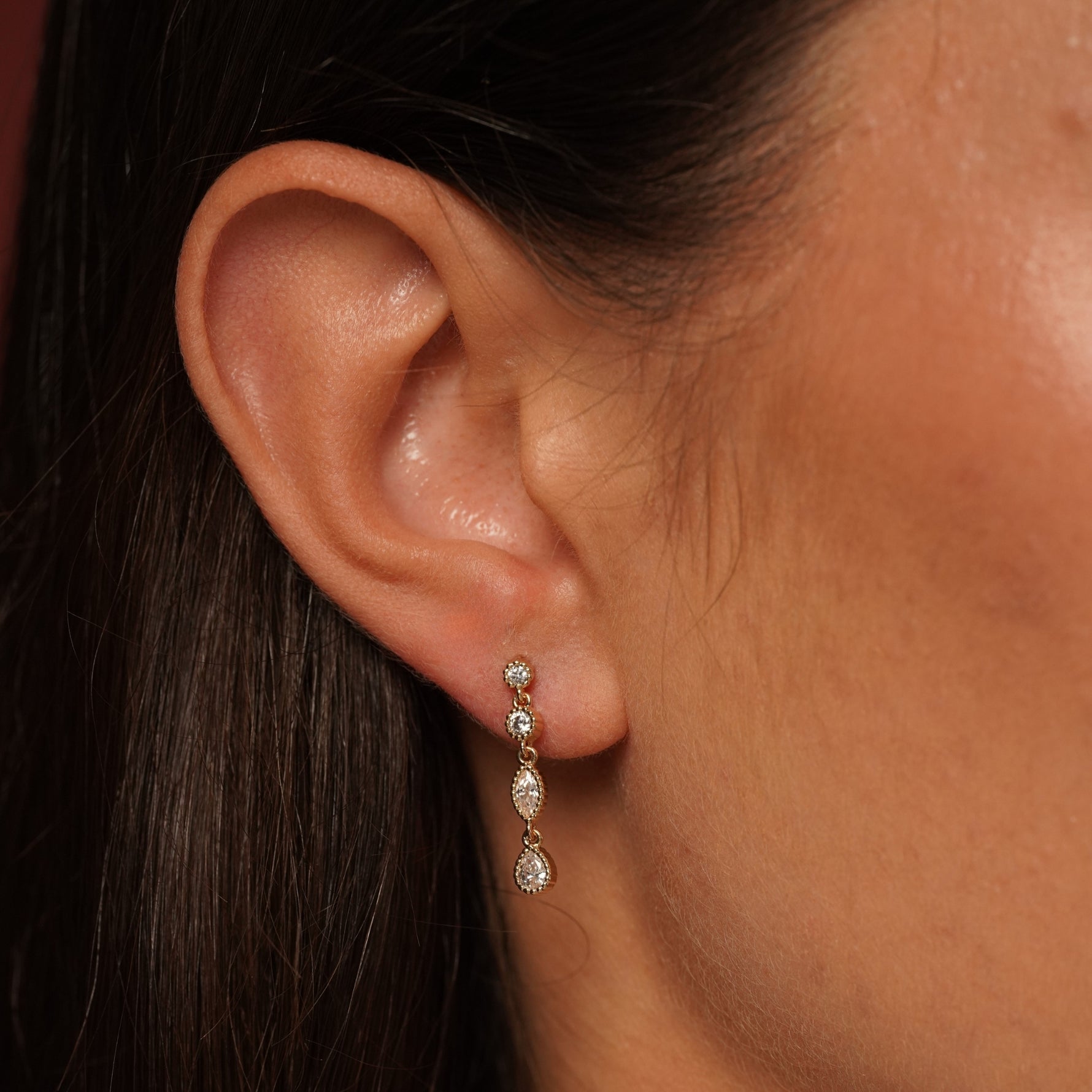 A close-up of a person's ear wearing Classic Cutness Earrings in 18K Gold Plating Featuring Round, Marquise and Pear Cut Cubic Zirconia Drop Earrings | Burren Jewellery