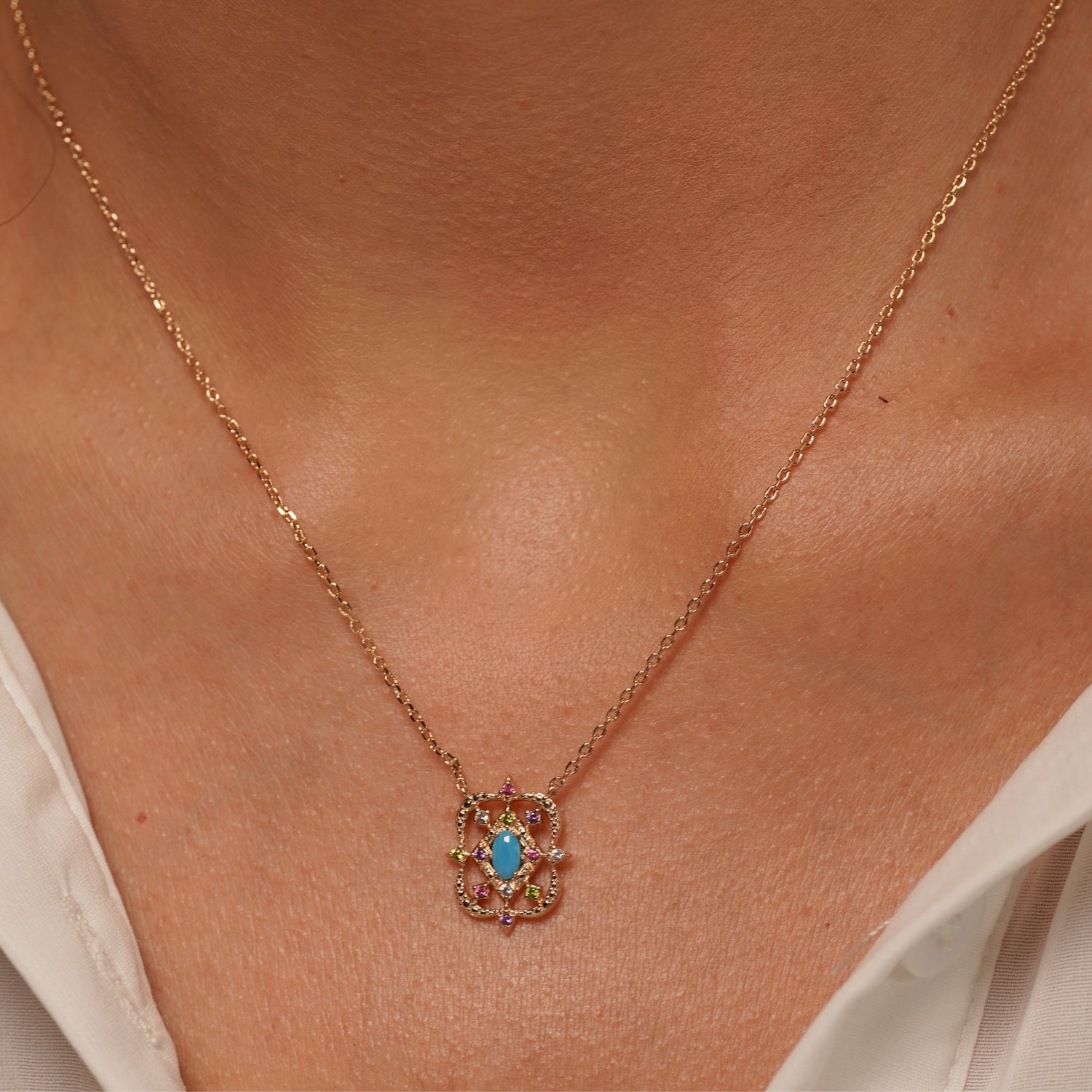 A close-up of a person's neck and collarbone wearing Desert Bloom Necklace in 18K Gold Plating Featuring a Turquoise-Coloured Oval Centre Stone with Multicolour Cubic Zirconia in an Intricate Openwork Pendant Design | Burren Jewellery