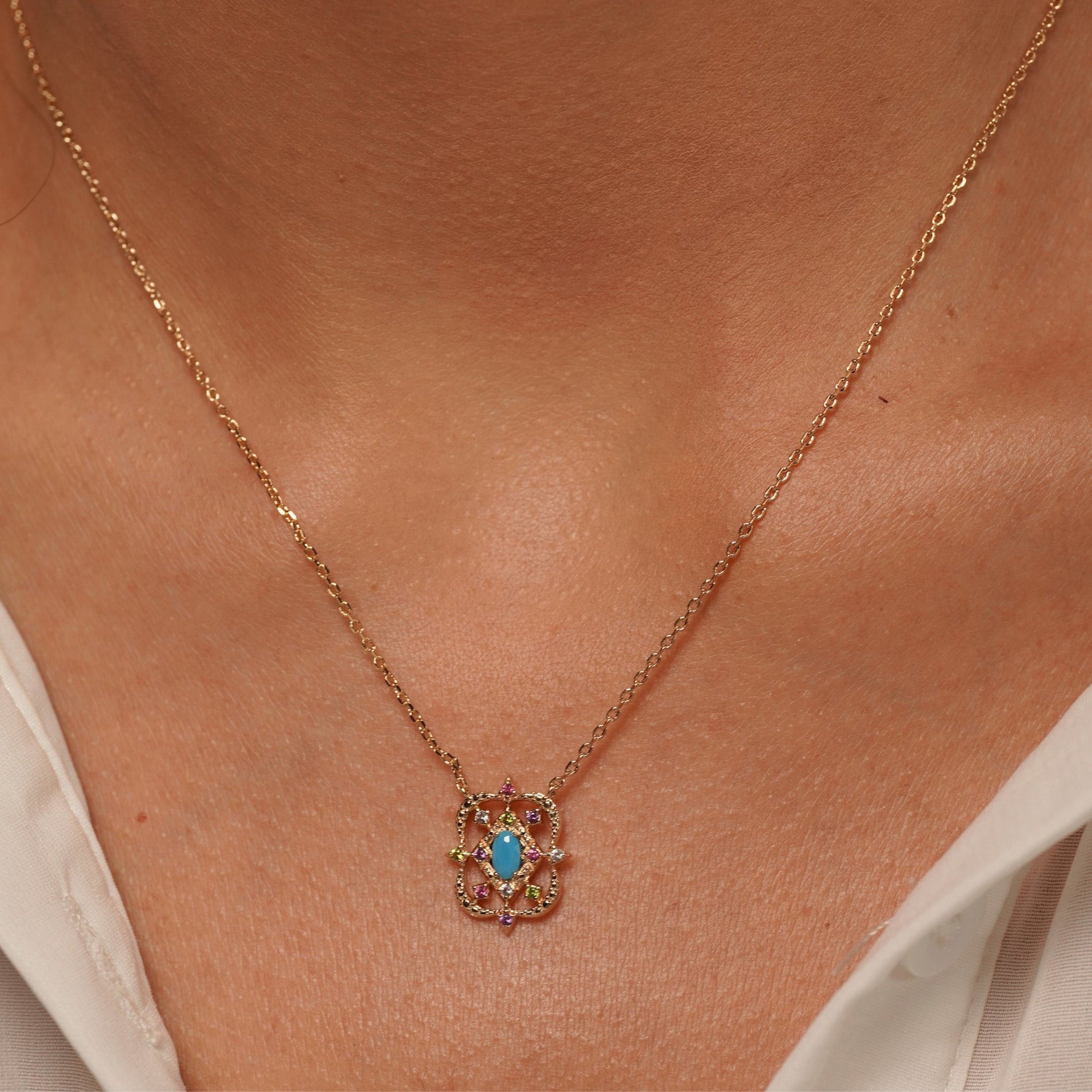 A close-up of a person's neck and collarbone wearing Desert Bloom Necklace in 18K Gold Plating Featuring a Turquoise-Coloured Oval Centre Stone with Multicolour Cubic Zirconia in an Intricate Openwork Pendant Design | Burren Jewellery