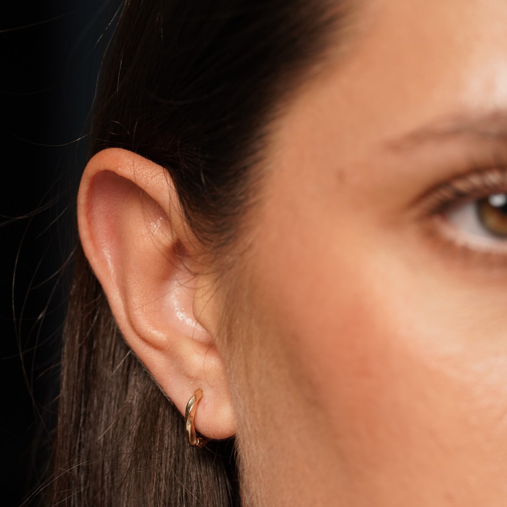 A close-up of a model's ear wearing Main Character Earrings in 18K Gold Plating Featuring Sculptural Twisted Huggie Hoop Design with a High-Polish Finish | Burren Jewellery