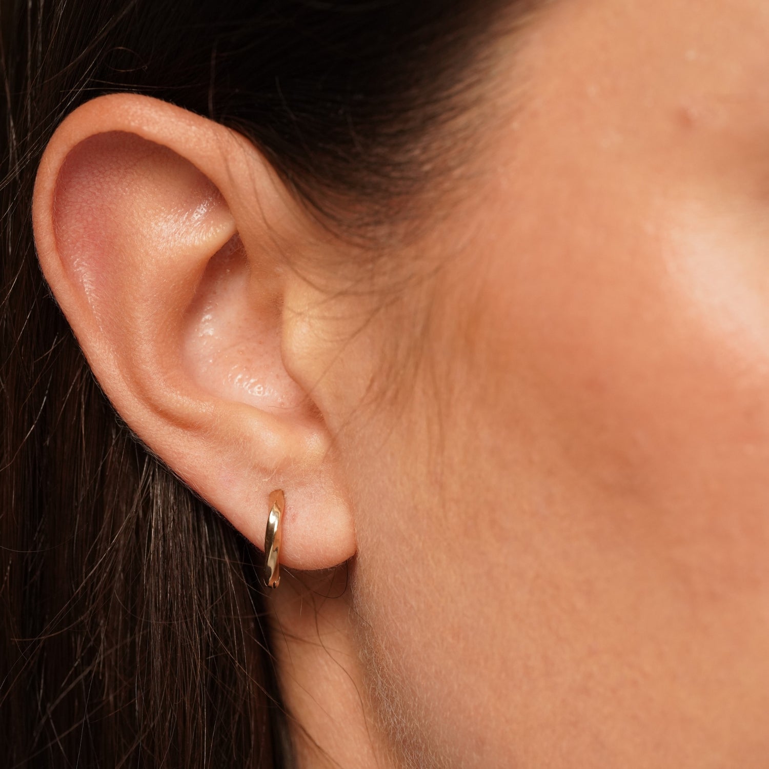 A close-up of a person's ear wearing Main Character Earrings in 18K Gold Plating Featuring Sculptural Twisted Huggie Hoop Design with a High-Polish Finish | Burren Jewellery