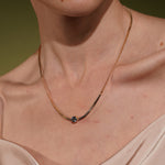 A close-up of a model's neck wearing the Marina Necklace in 18K Gold Plating Featuring a Bezel-Set Round Blue Cubic Zirconia Pendant on a Herringbone Snake Chain | Burren Jewellery