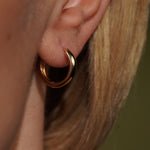 Close up of Model wearing in her ear Lily Huggies in 18K Gold Plating Featuring Smooth Polished Classic Hoop Earrings with a Secure Hinged Closure | Burren Jewellery