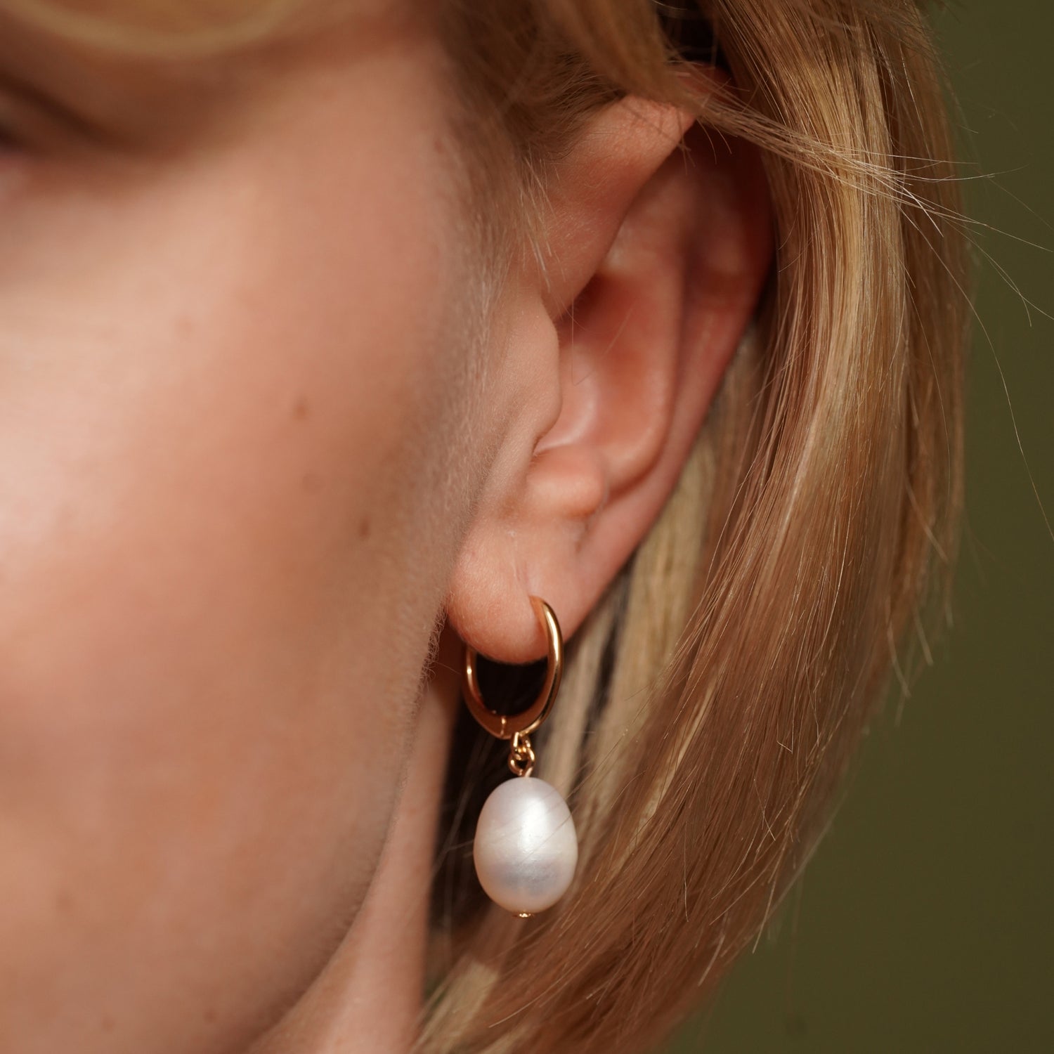 A close-up of a model's ear wearing Ocean Drop Earrings in 18K Gold Plating Featuring Genuine Freshwater Pearl Drop Huggie Earrings | Burren Jewellery
