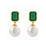 A pair of gold drop earrings featuring rectangular emerald-cut green gemstones and dangling baroque white pearls, set against a plain white background.