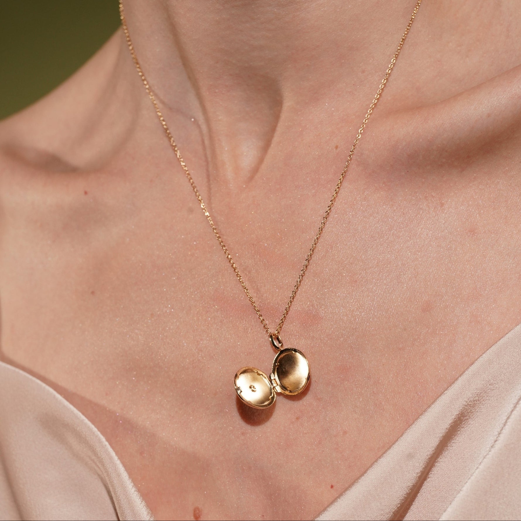 A close-up of a models's neck and chest wearing Little Moment Locket Pendant in 18K Gold Plating Featuring a Round Opening Locket with Cubic Zirconia Star Detail | Burren Jewellery