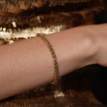 Model wearing the Sweet Echo gold plated wheat chain bracelet against a gold sequin backdrop