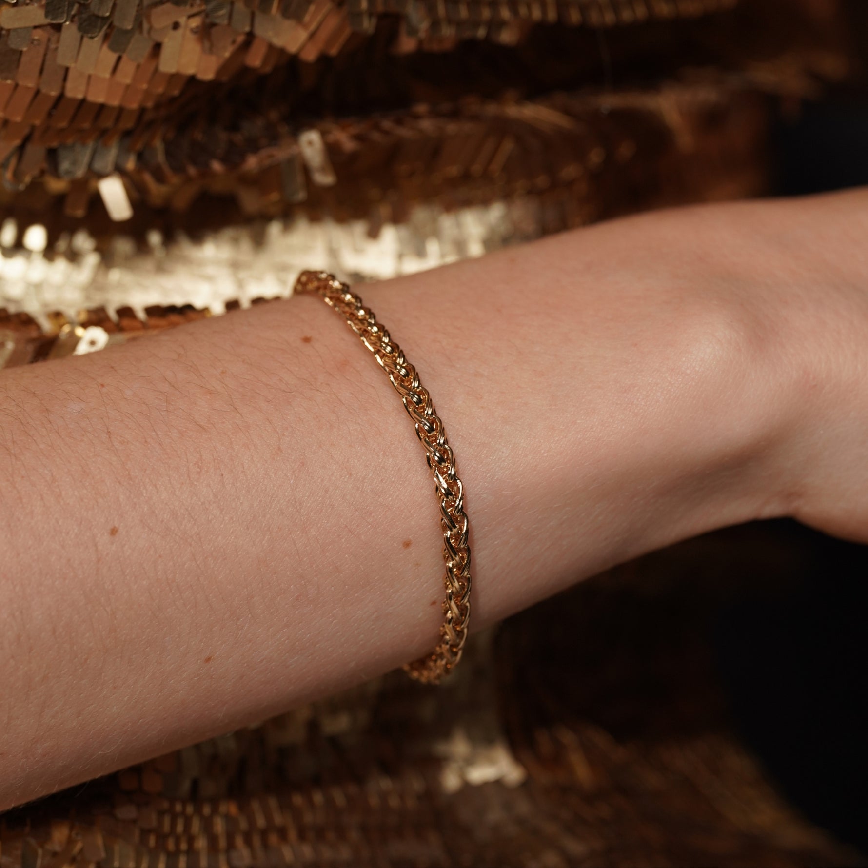 Model wearing the Sweet Echo gold plated wheat chain bracelet against a gold sequin backdrop