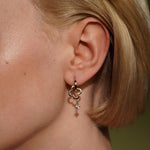 A close-up of a model's ear wearing Presence Earrings in 18K Gold Plating Featuring Open Clover Charms and Cubic Zirconia Drops | Burren Jewellery