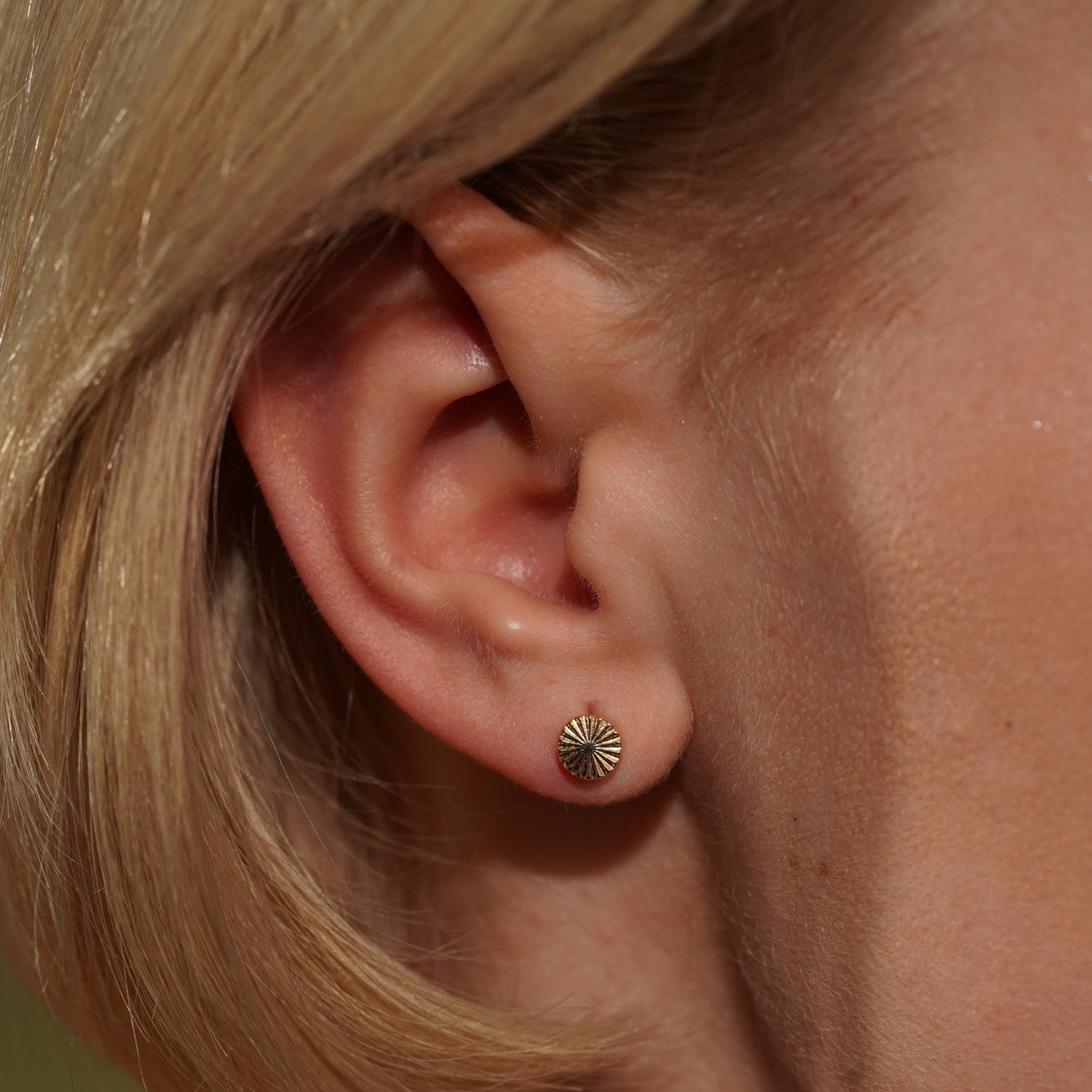 Close up of Models ear wearing the Radiance Earrings in 18K Gold Plating Featuring Engraved Sunburst Round Studs | Burren Jewellery
