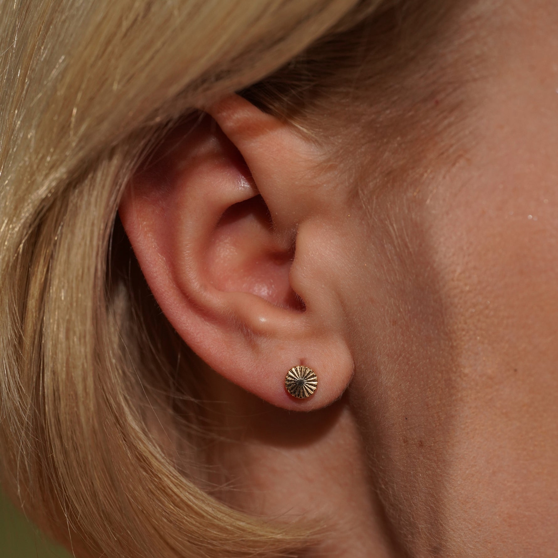 Close up of Models ear wearing the Radiance Earrings in 18K Gold Plating Featuring Engraved Sunburst Round Studs | Burren Jewellery
