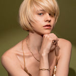 A close-up portrait of a blonde model wearing gold jewelry, including Golden Apology necklace and the Old Record 18K Gold Plated Mixed Link Chain Bracelet with Twisted Rope Detailing | Burren Jewellery
