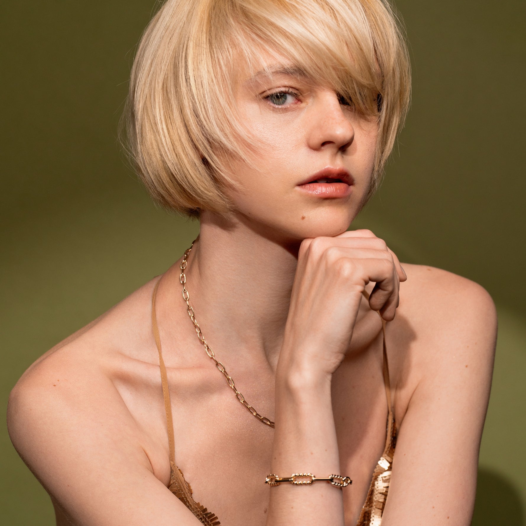 A close-up portrait of a blonde model wearing gold jewelry, including Golden Apology necklace and the Old Record 18K Gold Plated Mixed Link Chain Bracelet with Twisted Rope Detailing | Burren Jewellery
