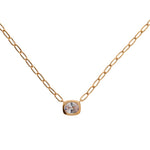 A delicate plated gold chain necklace with a small, bezel-set round clear gemstone pendant, displayed against a solid white background.