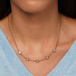 A close-up of a model wearing a delicate gold chain necklace with five small round clear gemstones spaced along the chain