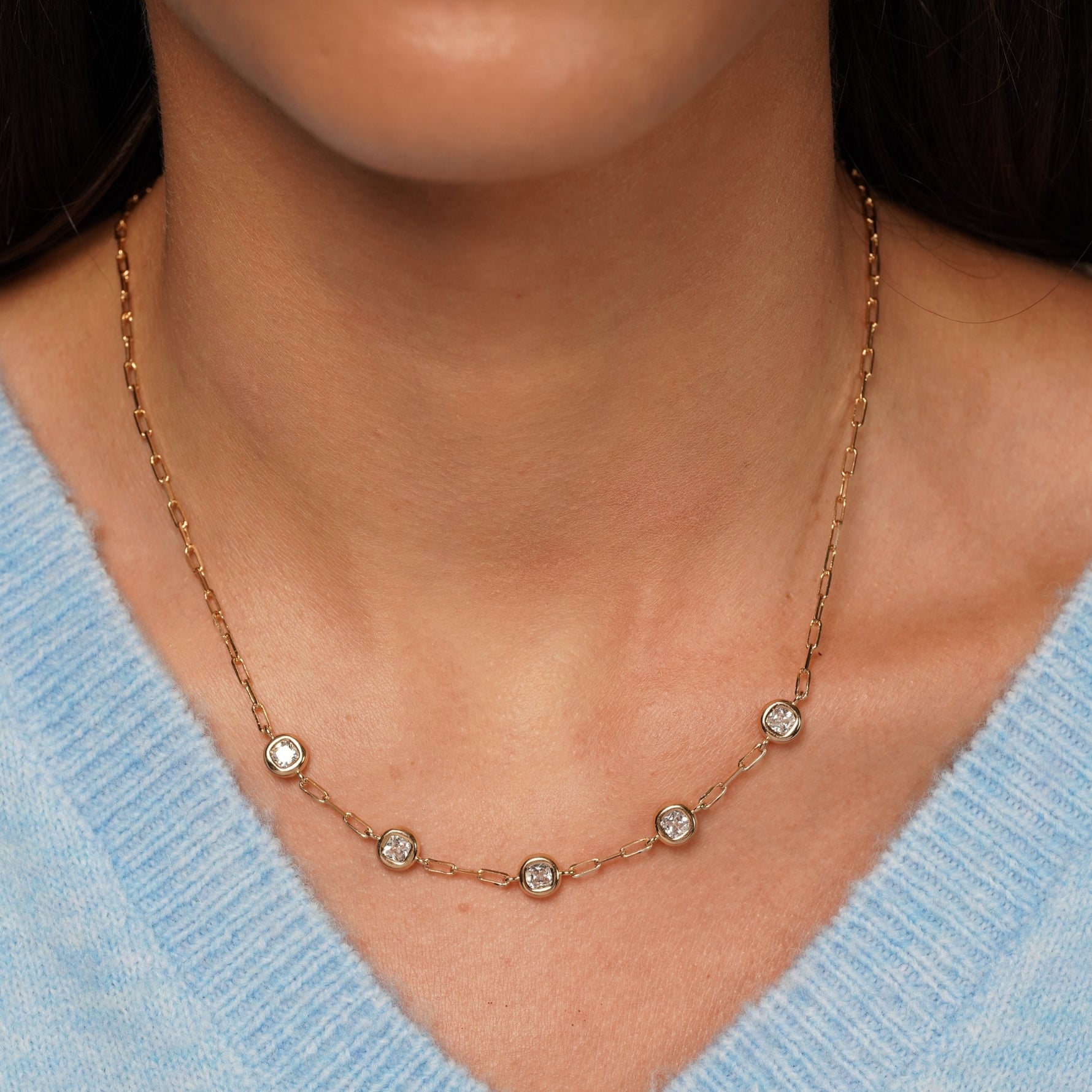 A close-up of a model wearing a delicate gold chain necklace with five small round clear gemstones spaced along the chain