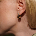 A close-up side shot of a models's ear wearing Sweetener oval huggie 18k gold plated burren jewellery 