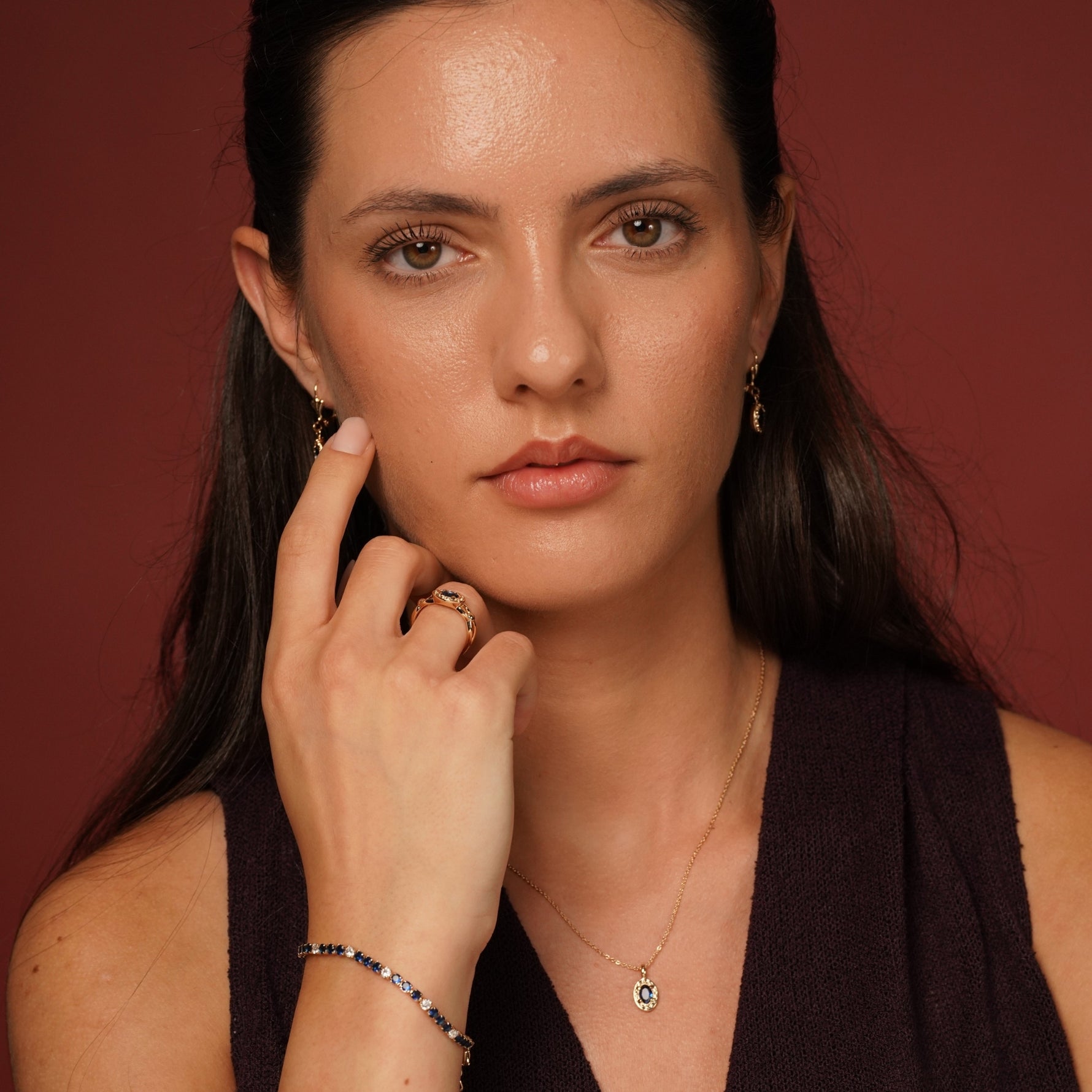 A close-up of a woman wearing delicate jewelry, including a small gold ring, a delicate gold necklace with a small green and white pendant, and a beaded bracelet