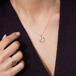 A close-up of a model wearing a delicate gold necklace featuring small blue and clear stones, paired with a matching ring on her finger.