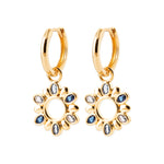 A pair of gold huggie hoop earrings with dangling sunflower charms, embellished with small blue and clear rhinestones, shown on a plain white background.