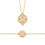 Gold jewelry set featuring a delicate chain necklace and a matching bracelet, both with a circular medallion pendant decorated with clear gemstones in a floral pattern.