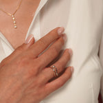 A close-up of a model's hand wearing Drifting Light Ring in 18K Gold Plating featuring an open flowing band with bezel-set cubic zirconia stones | Burren Jewellery