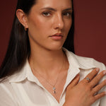 A close-up lifestyle shot of a woman wearing a delicate gold necklace with a dual-stone pendant and a matching gold ring on her finger.