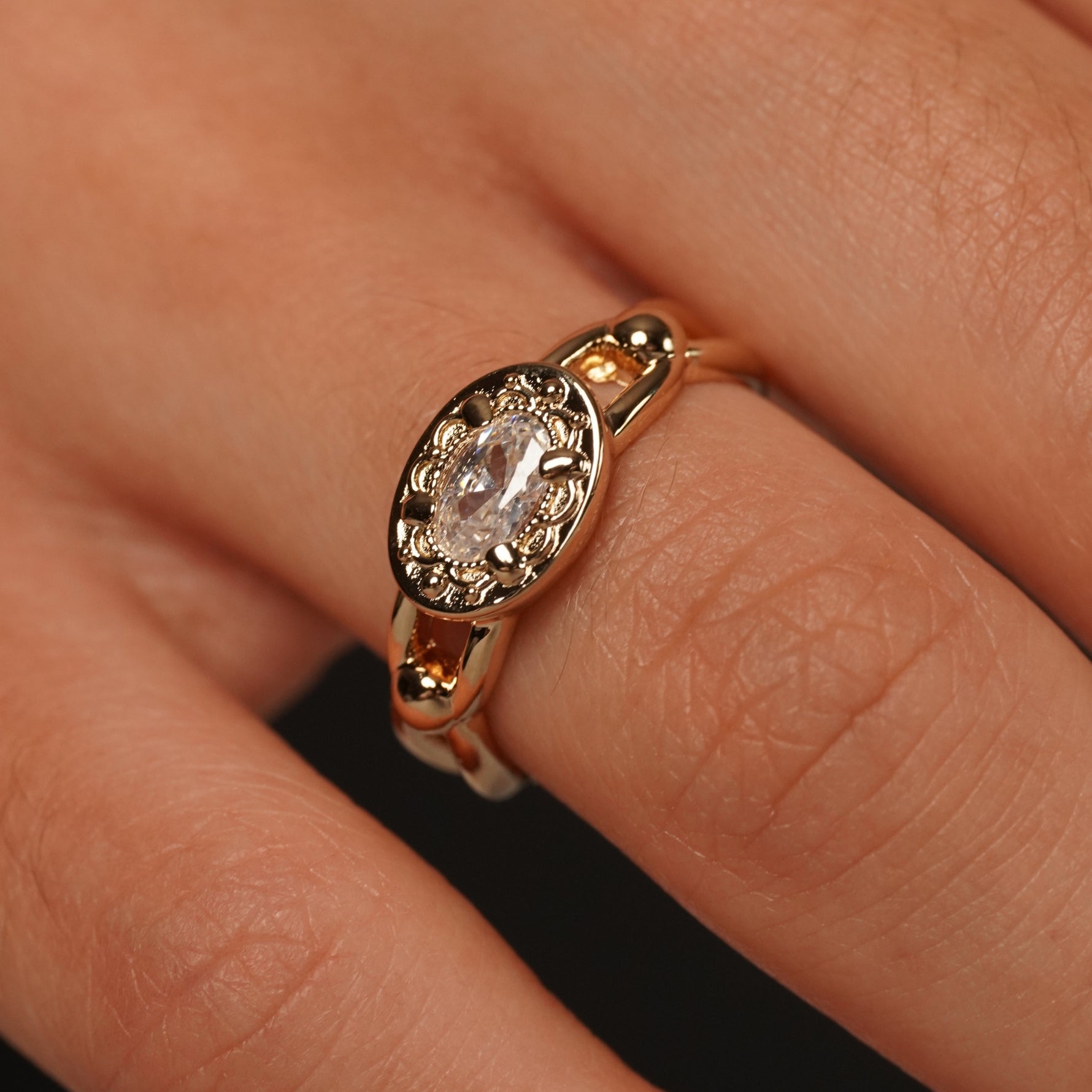 A close-up of a gold ring with an oval milky white gemstone and decorative filigree detailing, shown worn on a finger.