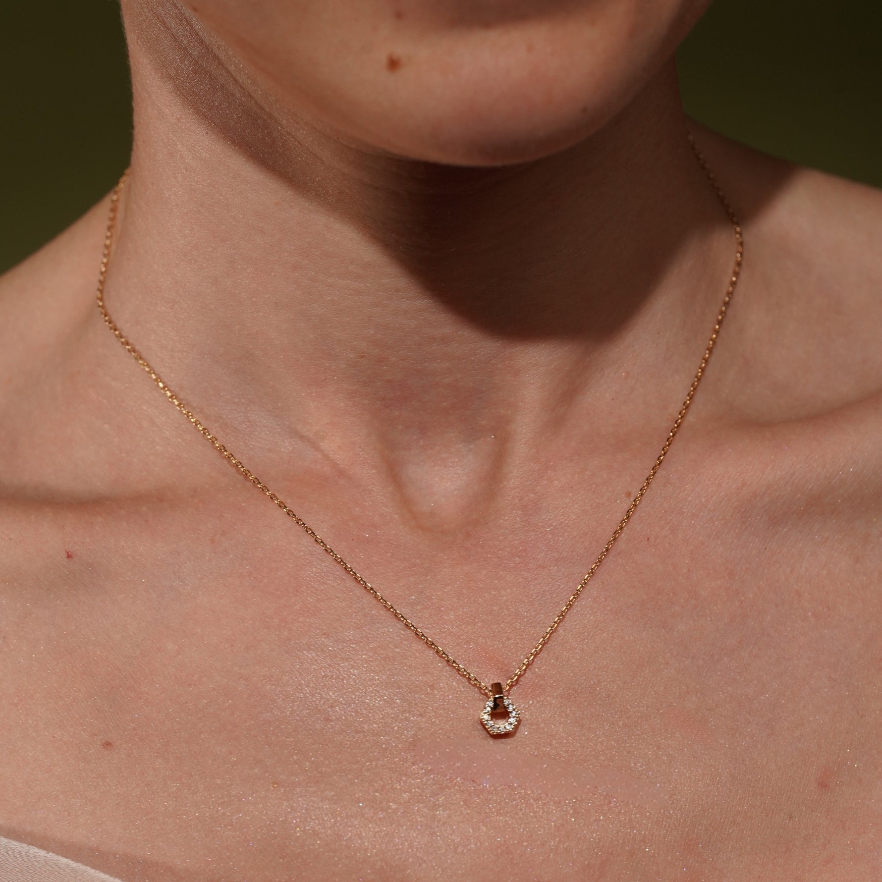 A close-up of a model's neck and chest wearing a delicate gold plated hexagonal pendant necklace with cz stone detail