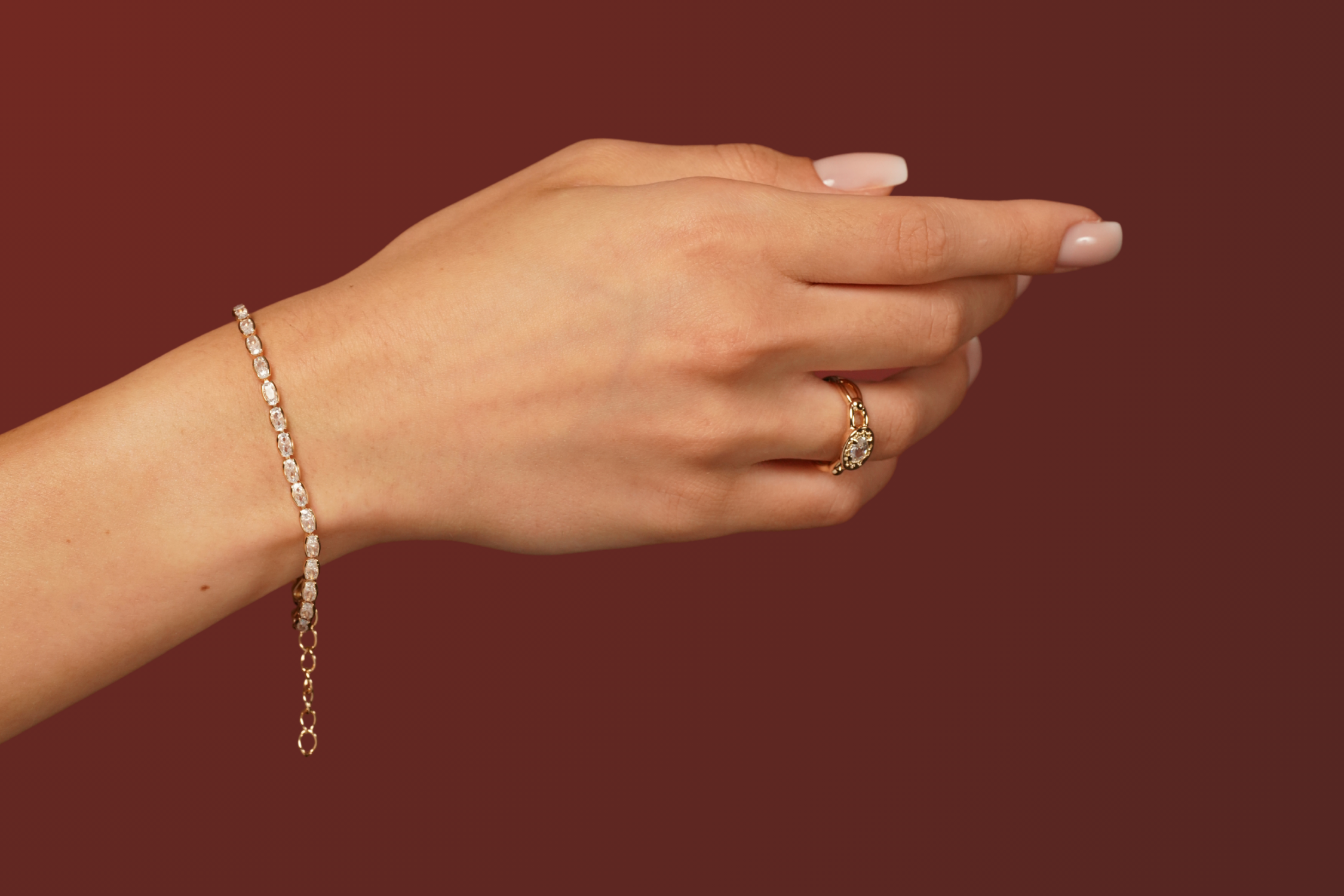 Nostalgia Ring and Radiant Eternity Bracelet in 18k gold plating with cubic zirconia by Burren Jewellery, styled on hand against a deep burgundy background.